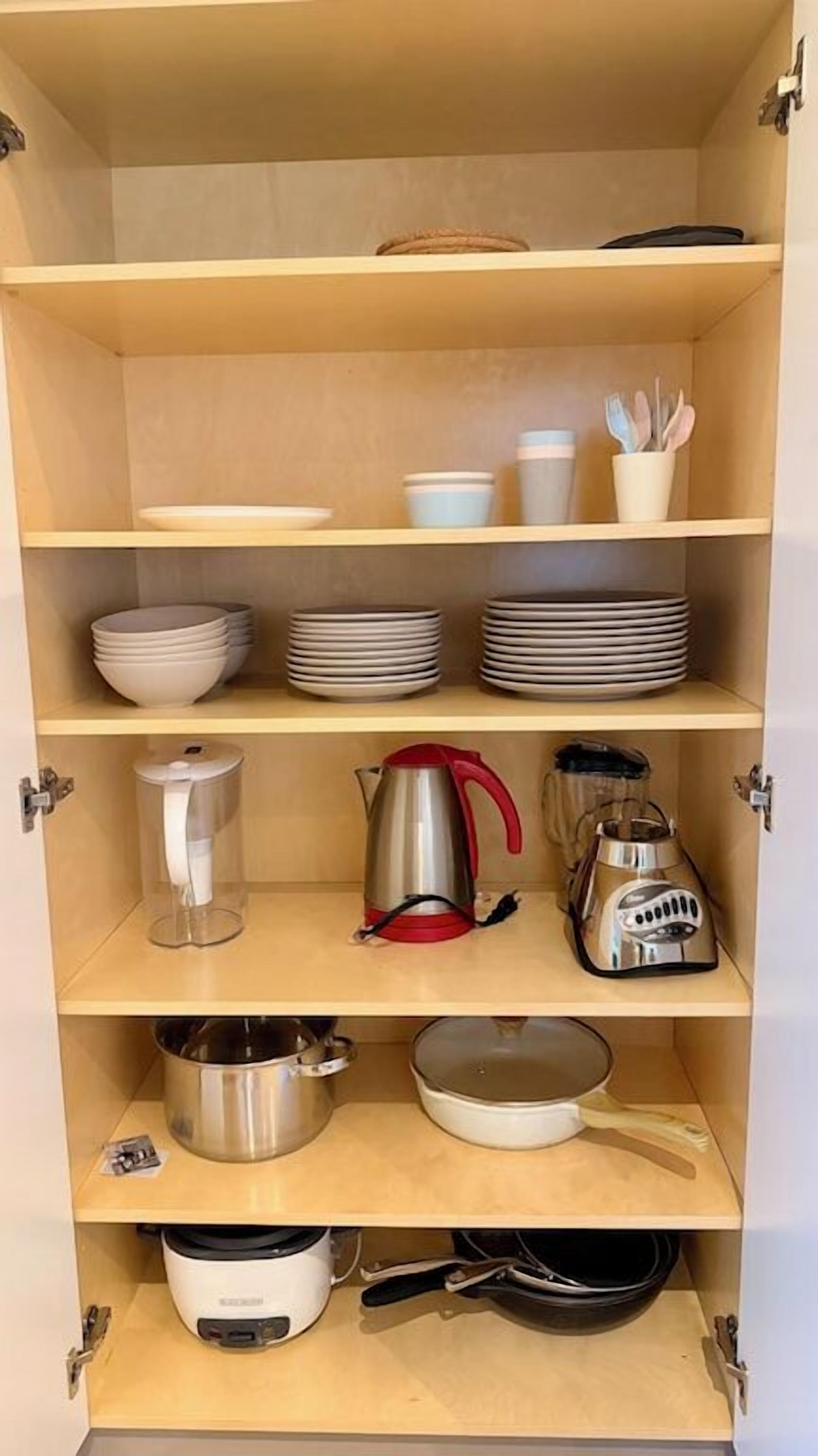 A kitchen with shelves holding plates, bowls, a kettle, a coffee maker, and pots.