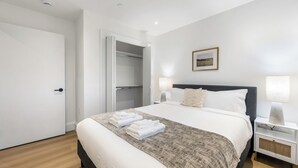 A neatly arranged bedroom with a bed, bedside lamps, a nightstand, and a wardrobe.