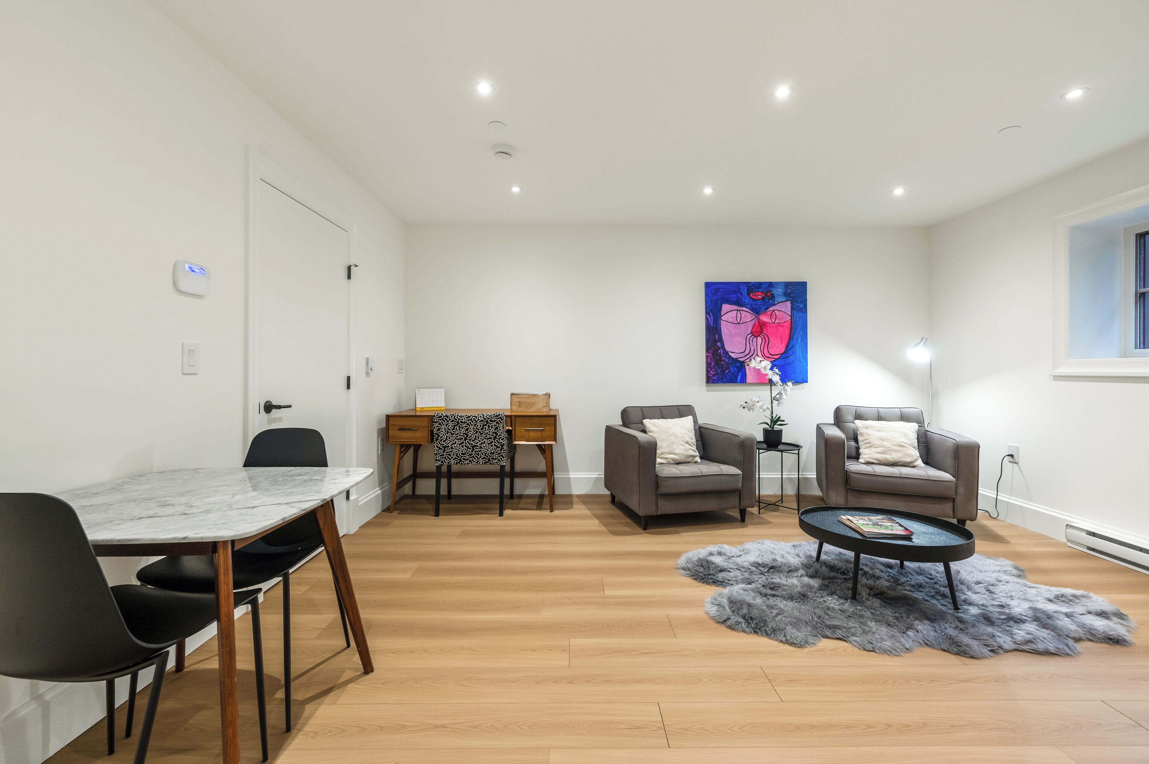 A modern living room with a dining area, two armchairs, a coffee table, and a painting on the wall.
