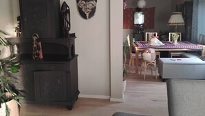 Een woonkamer met een donker houten kast, een decoratief masker aan de wand, een eettafel met stoelen en een lamp.