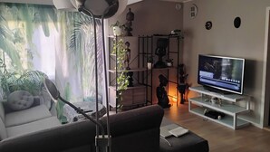 Een woonkamer met een bank, een tv op een dressoir, een vloerlamp en een muur met een muurschildering.