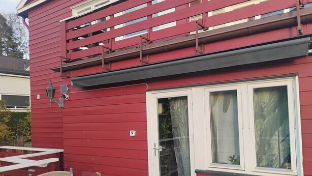 Een rood gebouw met een witte deur en ramen, een klein terras met een stoel en een metalen hekwerk.