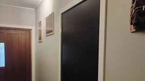 Een gang met een houten deur, een zwarte deur en twee ingelijste foto's aan de muur.