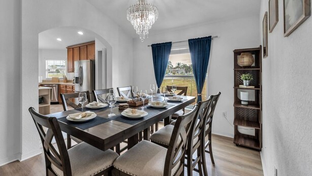 A dining area with a chandelier, a view of the outdoors, and a kitchen in the background. - Dinner Lake Home | Sunset Views | Extended Stay | 4BR, Sleeps 8, Near Legoland (Lake Wales)
