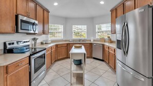 A modern kitchen with wooden cabinets, stainless steel appliances, and a central island. - Dinner Lake Home | Sunset Views | Extended Stay | 4BR, Sleeps 8, Near Legoland (Lake Wales)