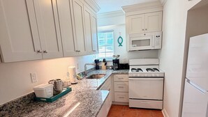 Una cocina con armarios blancos, encimera de granito, estufa, microondas y refrigerador.