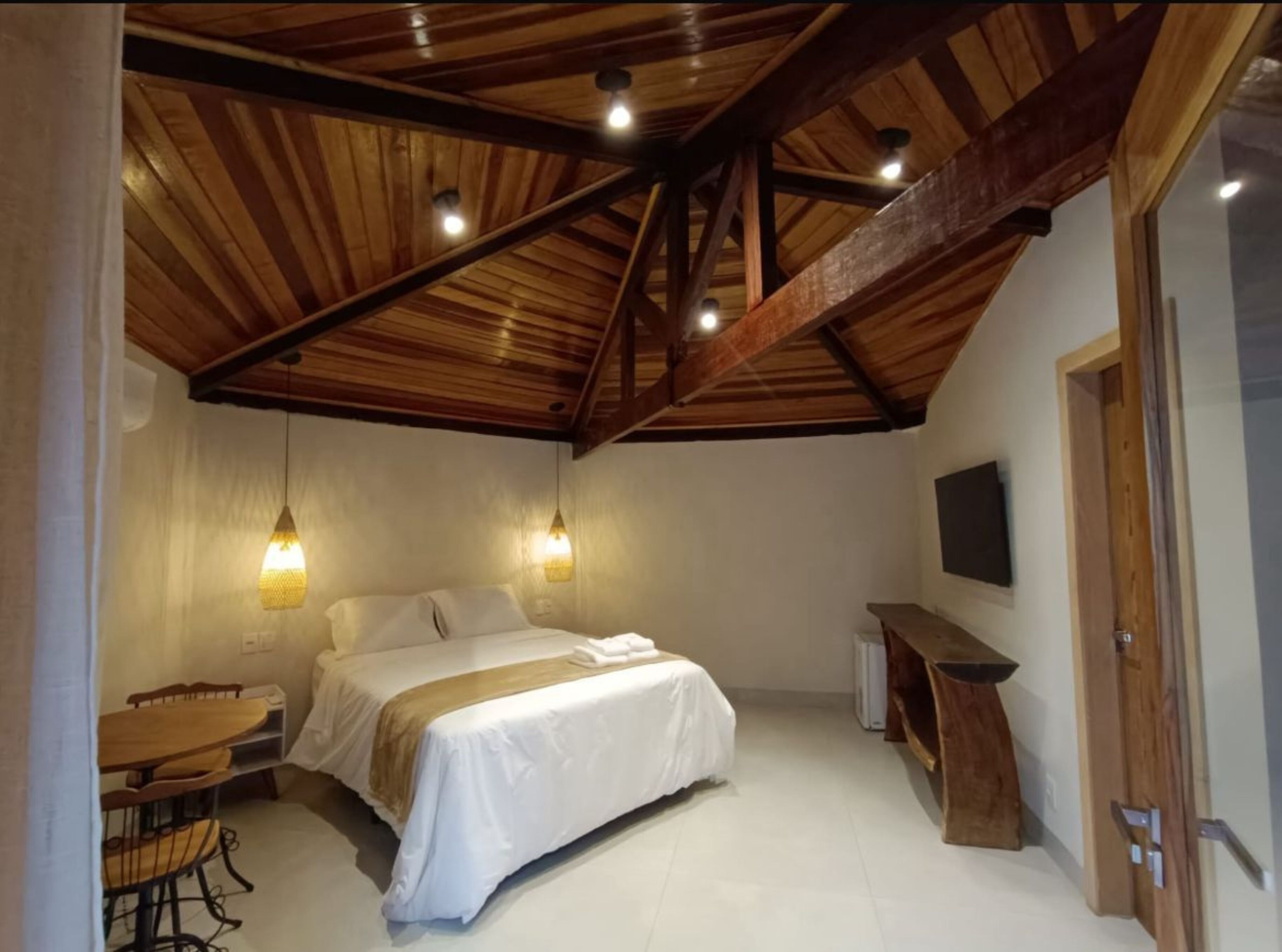 Un dormitorio con techo de madera, una cama, un escritorio y un televisor.