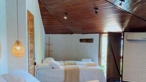 A hotel room with a sloped ceiling, two beds, a hanging light fixture, and a large window.