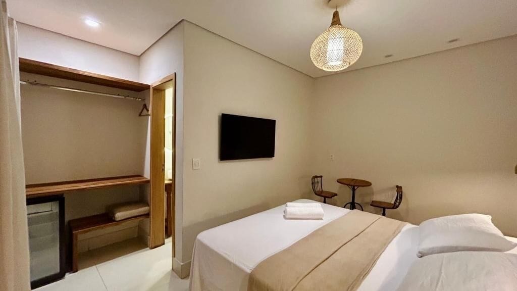 A hotel room with a bed, a TV, a wardrobe, and a small table with chairs.