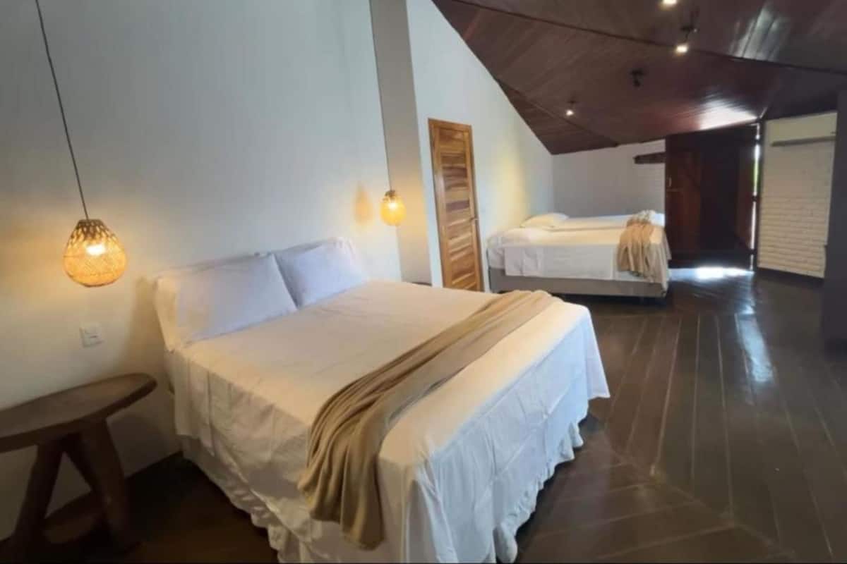 Habitación con dos camas, suelo de madera, techo inclinado e iluminación colgante.