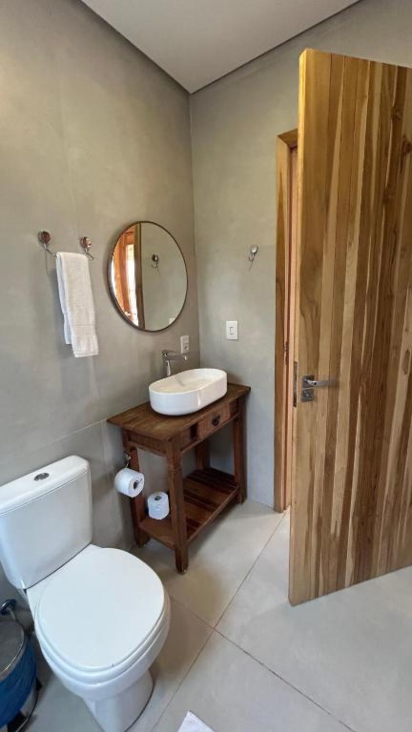 Un baño con inodoro, lavamanos, tocador de madera y puerta de madera.