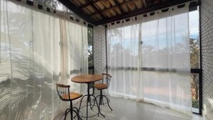 A room with a brick wall, a wooden table, two chairs, and sheer curtains.