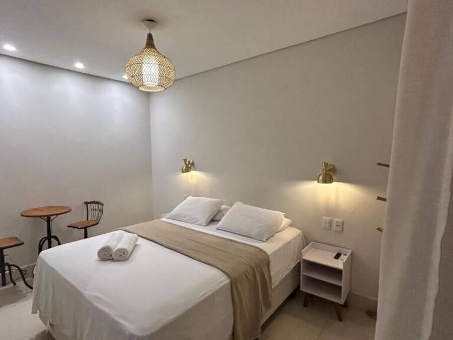 A hotel room with a bed, bedside tables, a lamp, a chair, and a small table.