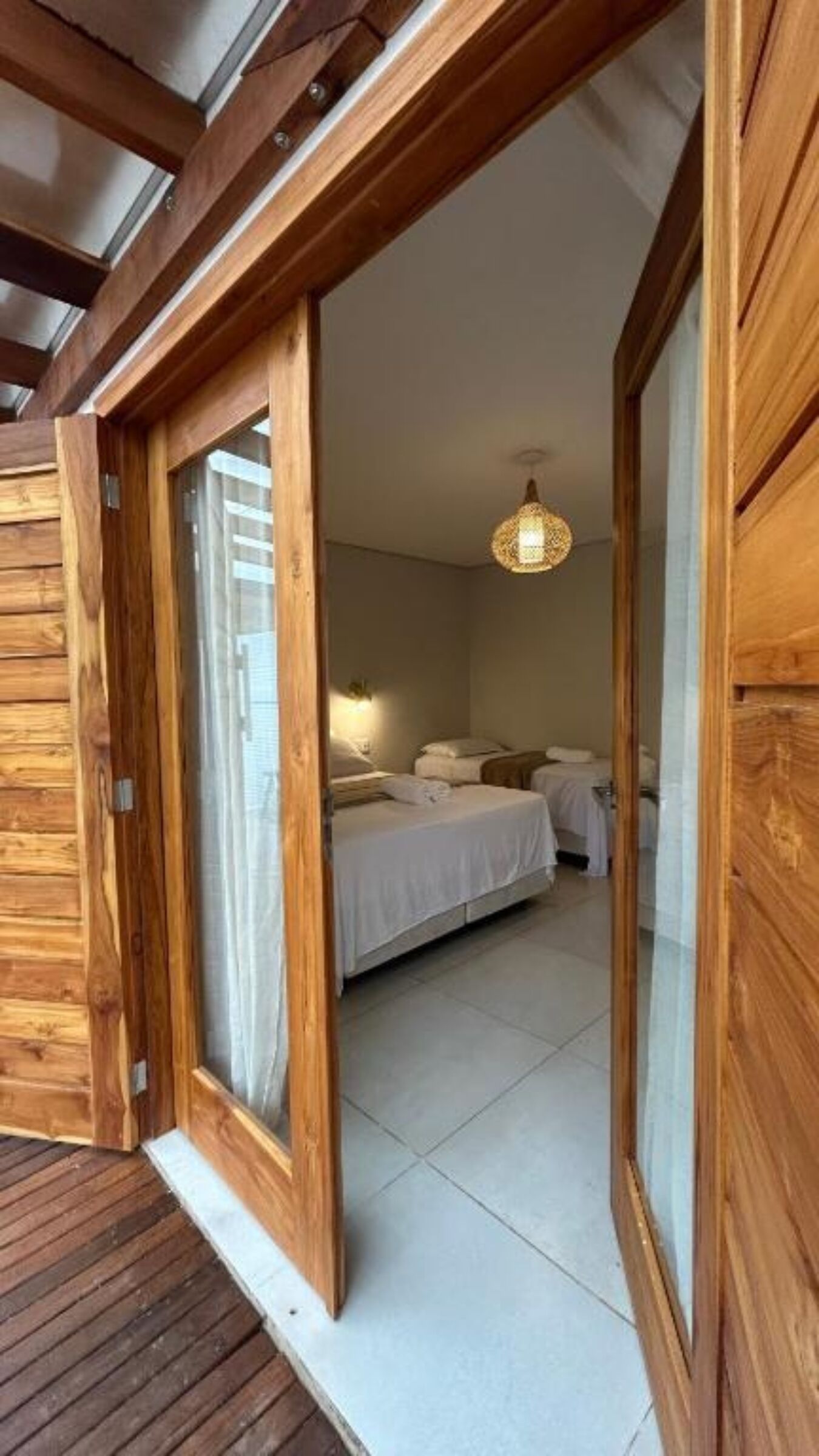 A wooden room with a bed, a hanging light fixture, and a sliding door.