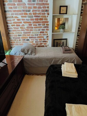 A room with a brick wall, a bed with striped bedding, a black sofa, and a wooden dresser. - Luxury One Bedroom Apartment in the Center of Tallinn Old Town (Tallinn)