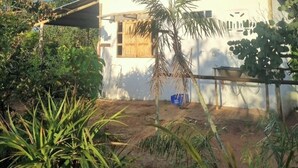 A house with a white exterior, a wooden door, and a small garden with various plants. - New house in the heart of the Cerrado biome, easy access and 5 minutes from several waterfalls. (Alto Paraíso de Goiás)