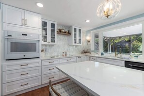 A modern kitchen with white cabinetry, a large island, and a view of the outdoors. - Waterfront Getaway with Boat Slip (Ocean Pines)