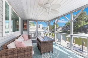A covered outdoor deck with wicker furniture, a table, and a view of a body of water. - Waterfront Getaway with Boat Slip (Ocean Pines)