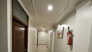 Un couloir avec un extincteur fixé au mur, une porte sur la gauche et un luminaire au plafond.