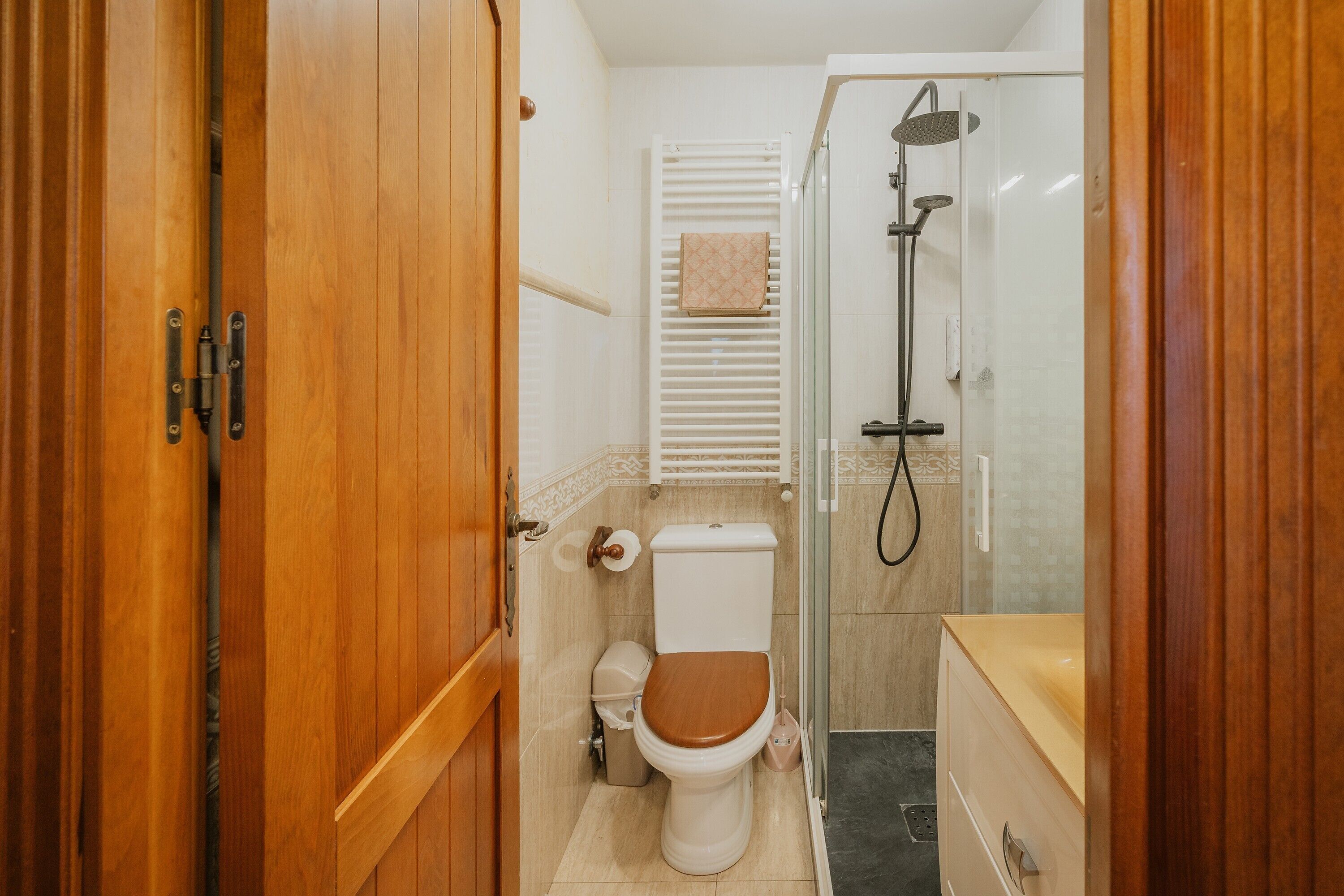 A bathroom with a wooden door, a toilet, a shower, and a towel rack.