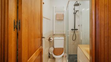 A bathroom with a wooden door, a toilet, a shower, and a towel rack.