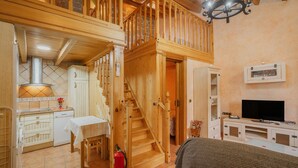 A wooden staircase connecting two floors, a kitchen with a stove, a dining table, and a television in a cozy room.