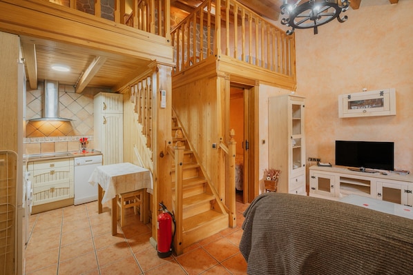A wooden staircase connecting two floors, a kitchen with a stove, a dining table, and a television in a cozy room.