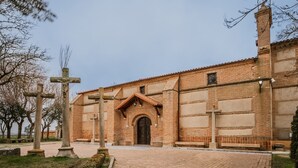 A brick building with a central arched entrance, multiple crosses, and a paved courtyard.