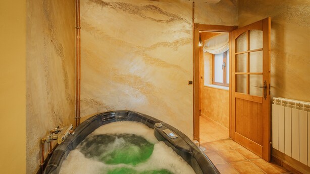A hot tub with visible pipes and a control panel, a wooden door with glass panels, and a tiled floor.