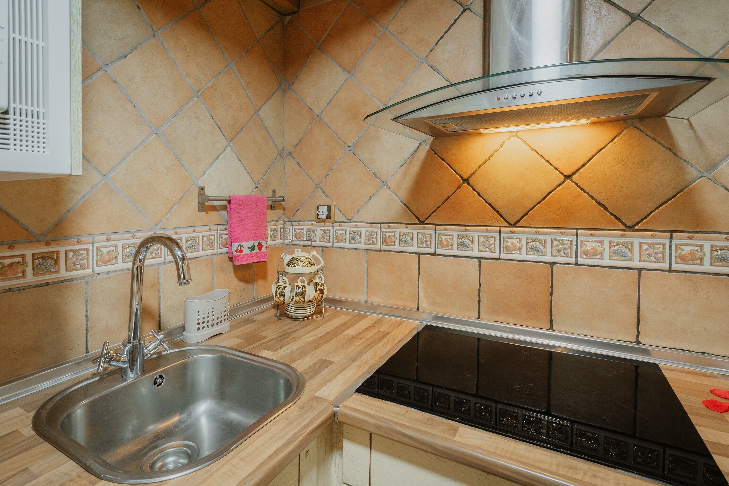 Cocina con pileta de acero inoxidable, lavavajillas negro, extractor de acero inoxidable y salpicadero de azulejos.
