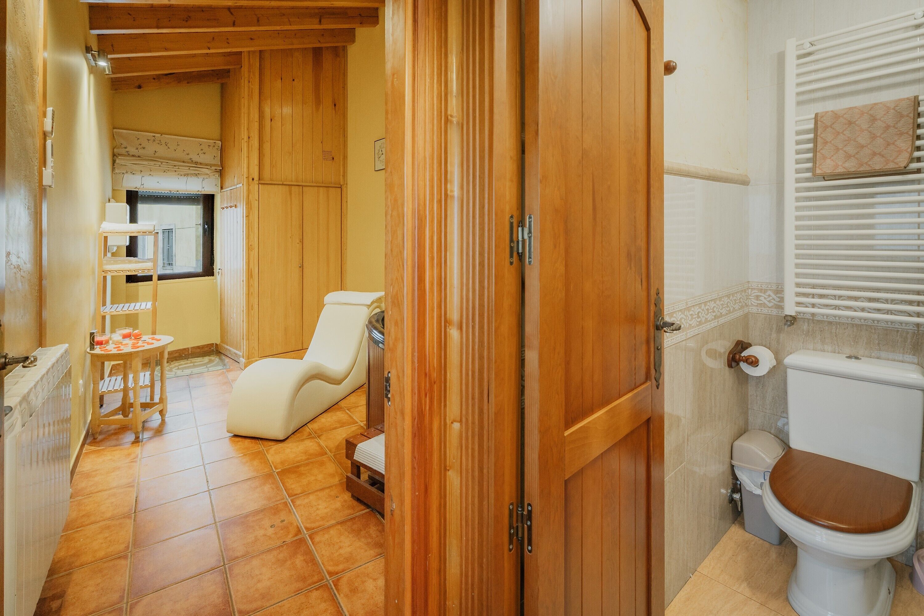Et badeværelse med en trædør, toilet, bruseområde og et vindue med gardin.