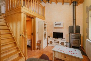 A wooden staircase leading to a loft, a television, a wood-burning stove, and a dining table with rose petals.