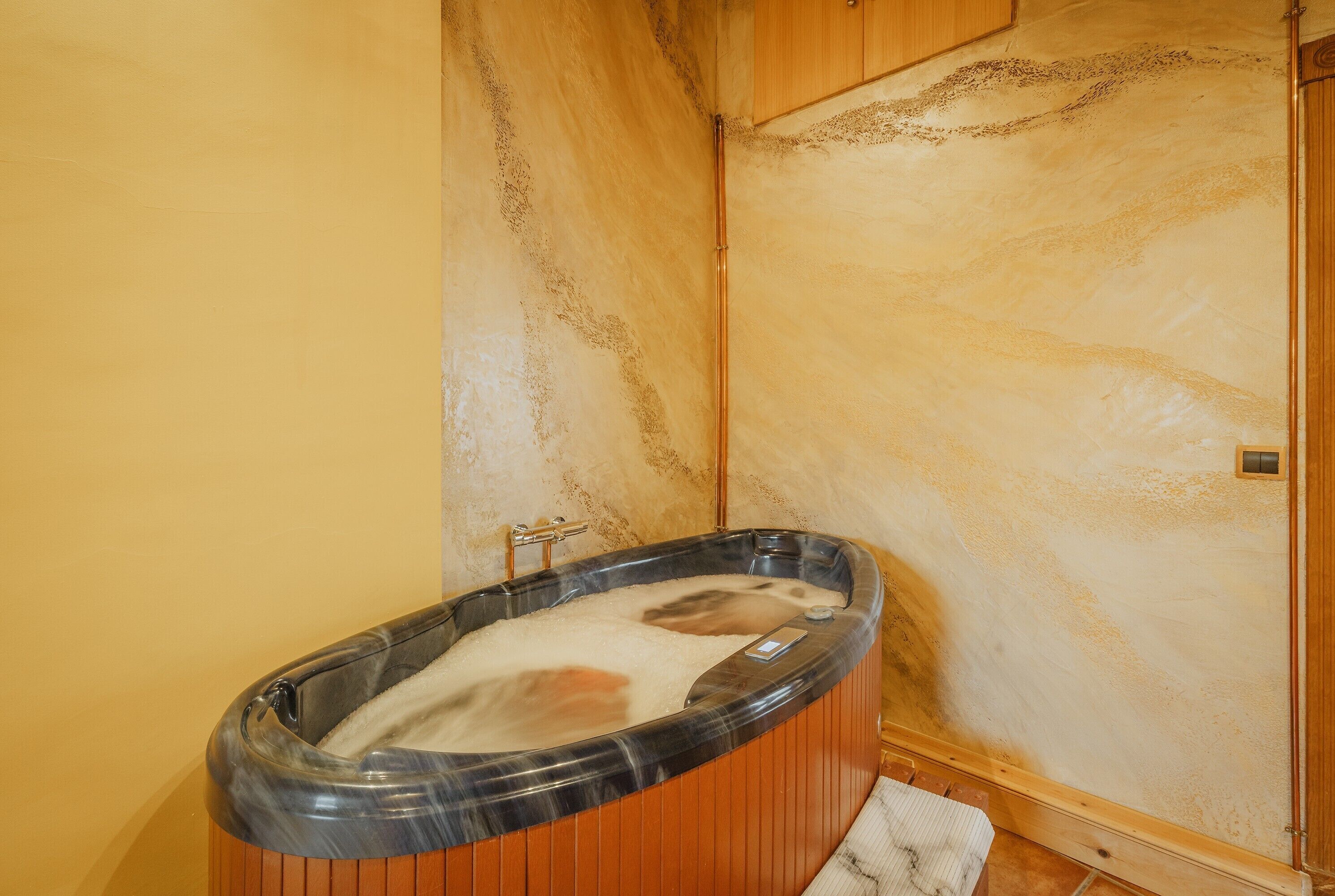 A bathroom with a wooden bathtub, a towel, and a marble wall.