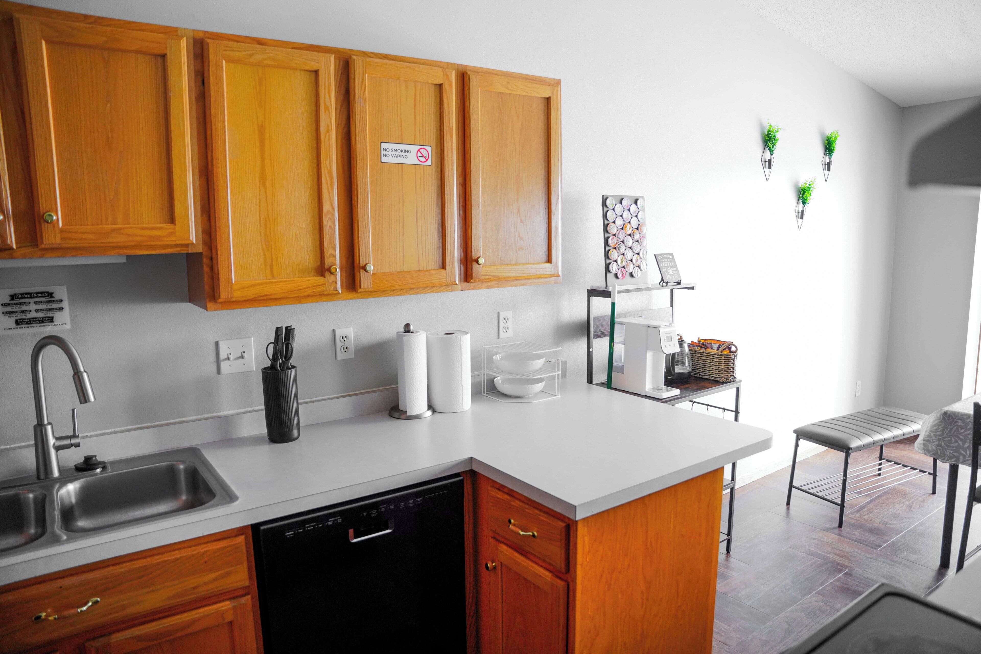 A kitchen with wooden cabinets, a dishwasher, a sink, a countertop with a basket, and a wall-mounted plant.