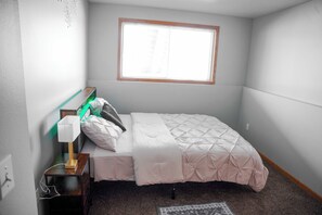 A bedroom with a bed, a bedside table with a lamp, a window, and a carpeted floor. - Family & Work-Friendly, Backyard & Garage, Near Sanford & West Acres, Breakfast (Fargo)