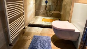 Une salle de bain avec une douche à parois de verre, des toilettes blanches, un porte-serviettes avec des serviettes pliées et un tapis de bain bleu.