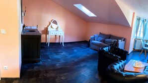 Une chambre à coucher confortable, aménagée en mezzanine avec un plafond en pente, comprenant une coiffeuse avec un miroir, un canapé en cuir noir et une table à manger.