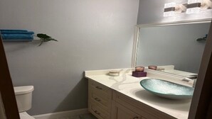 A bathroom with a white toilet, a beige vanity with a glass bowl sink, and a mirror above the sink. - Stay Where Tampa Comes Alive - Central Home Near Events & Attractions (Tampa)