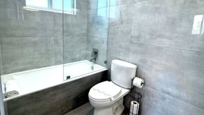 Et moderne badeværelse med en glasafskærmet brusebad, et hvidt toilet og et badekar.