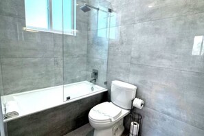 A modern bathroom with a glass-enclosed shower, a white toilet, and a bathtub. - Driftwood Hideaway 1 Bedroom (Lauderdale-by-the-Sea)
