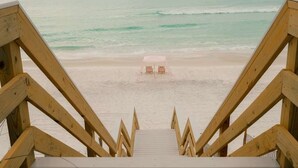 Una escalera de madera que lleva a una playa con un área de descanso techada.