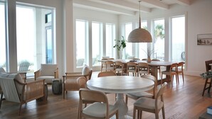 Un comedor amplio con una mesa redonda y varias sillas, ventanas grandes y una lámpara colgante.