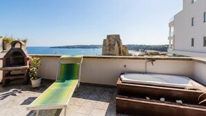 Une terrasse sur le toit offrant une vue sur la mer, une structure en pierre, un barbecue, un fauteuil de relaxation et un jacuzzi.