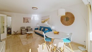 A spacious living room with a blue sofa, a round coffee table, and a dining area with chairs. - HENRI CAMILLE RE - Passy1 -Beautiful one bedroom swimming pool and parking (Cannes)