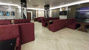 A modern hotel lobby with red seating, a reception desk, and a large TV screen. - Hotel Sea Touch (Kanthi)