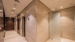 Moderni hotellikäytävä, jossa on lasiseinällä erotettu suihku, puuseinä ja laatoitettu lattia.