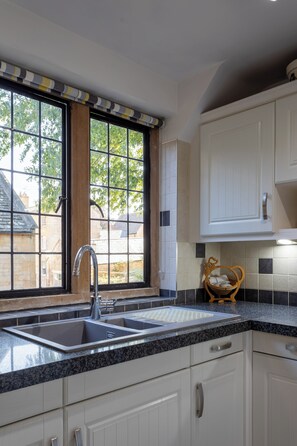A kitchen with a double sink, white cabinets, and a window with a view of buildings and trees.