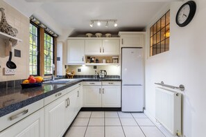 A kitchen with white cabinets, a black countertop, a white refrigerator, and a wall clock. - Authentic & Stylish Gem in the Heart of Chipping Campden: Toys, Books, Workspace (Chipping Campden)