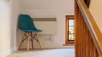 Un escalier dont les marches sont recouvertes de moquette mène à un palier. Une chaise de couleur turquoise est placée sur le palier, et un radiateur blanc est fixé au mur.