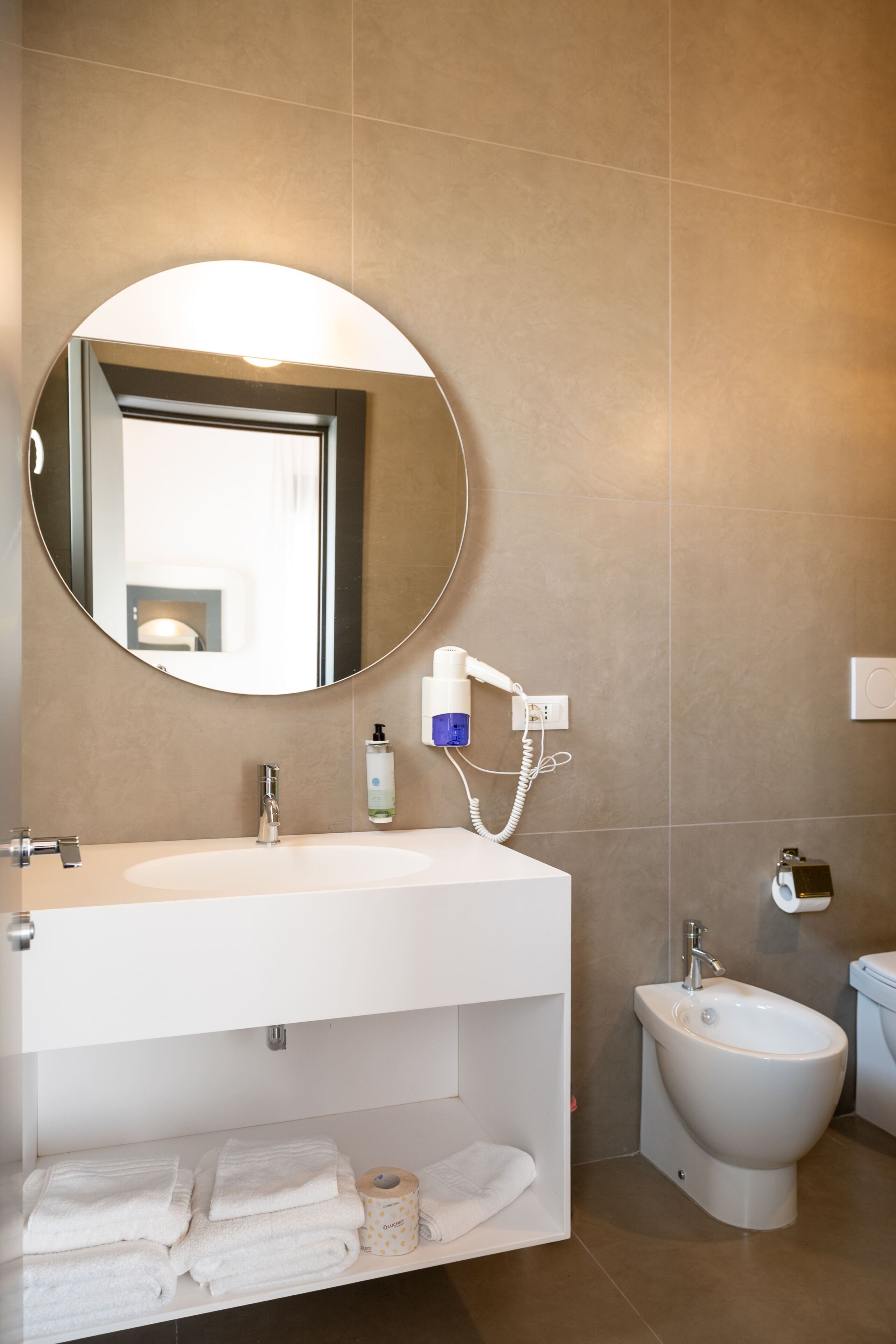 A bathroom with a white sink, a round mirror, a bidet, and a toilet.